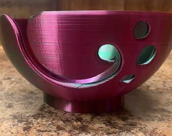 May include: A magenta yarn bowl with a treble clef design and multiple holes for yarn to feed through.