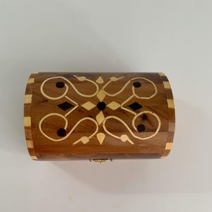 Peut inclure: Un coffret en bois avec un dessus incurvé, orné d'un motif incrusté de bois clair et foncé. Le coffret est doté d'un fermoir en laiton et est fait de différentes teintes de bois, dont le marron clair et foncé.