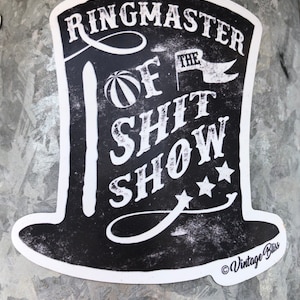 May include: Black and white sticker of a top hat with the text "Ringmaster of the Shit Show" and three stars. The sticker has a copyright symbol and the text "Vintage Bliss".