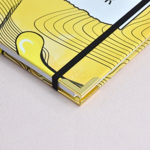 Up close view of gold corners with elastic holder. Yellow cover with close up of swirl design, graphics.