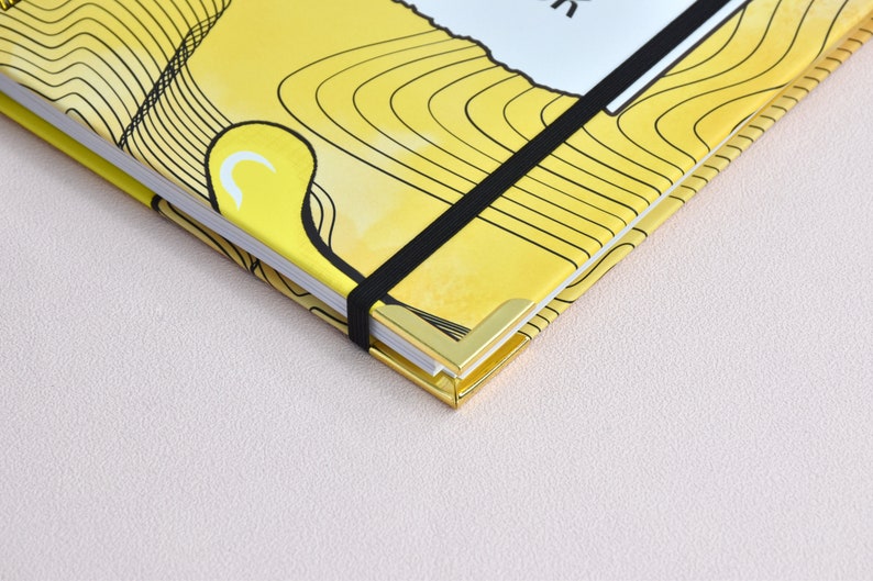 Up close view of gold corners with elastic holder. Yellow cover with close up of swirl design, graphics.