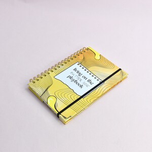 Yellow, guided journal lying flat on a surface, enhanced with gold binding, gold corners, elastic holder.