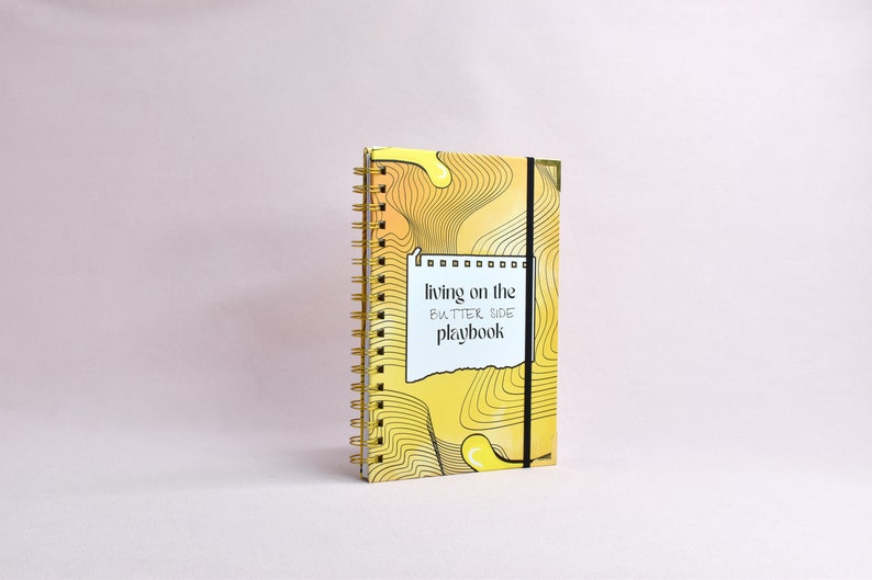 Side view of yellow, guided journal enhanced with gold binding, gold corners, elastic holder.