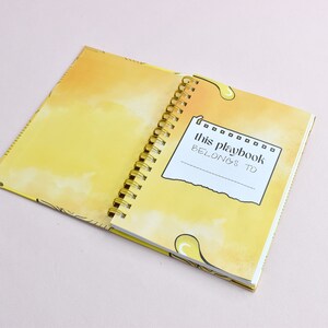 Guided journal displays the inside of the cover page, the page where you write the name of who the journal belongs to. Pages are yellow with yellow graphics; gold binding.