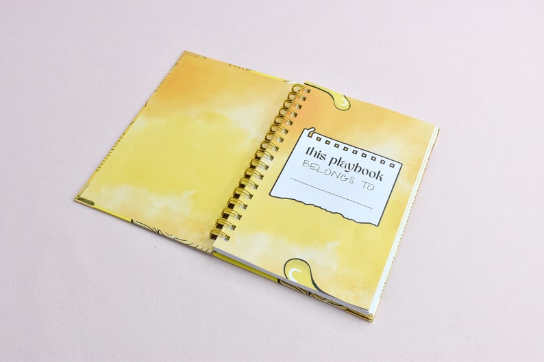 Guided journal displays the inside of the cover page, the page where you write the name of who the journal belongs to. Pages are yellow with yellow graphics; gold binding.