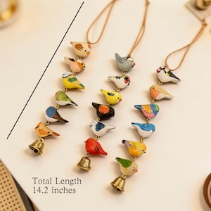 May include: A collection of colourful, hand-painted wooden bird ornaments, each suspended by a brown cord. Each bird is unique in colour and design, with a small gold bell at the bottom. The total length is 36 cm.