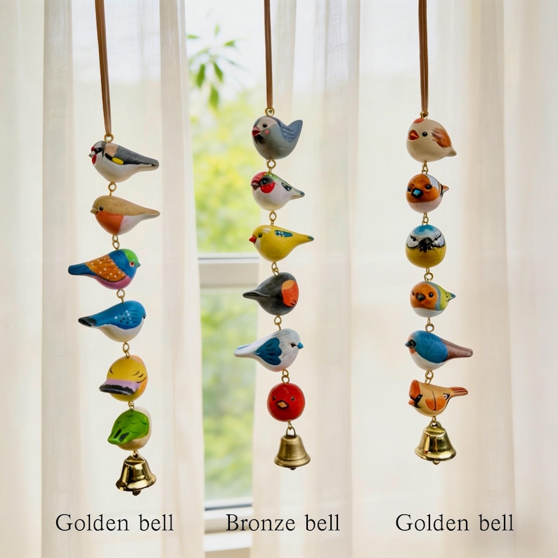 May include: Three hanging bird wind chimes. Each chime features a series of colourful, painted wooden birds strung together, with a bell at the bottom. The chimes are suspended from brown cords. The text "Golden bell" and "Bronze bell" are at the bottom.