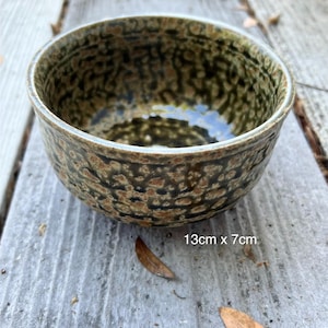 May include: A ceramic bowl with a speckled brown and green pattern. The bowl is round with a slightly flared rim. The dimensions are 5.1 inches in diameter and 2.8 inches in height.