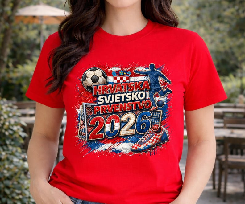 May include: Red t-shirt featuring a soccer-themed graphic. The design includes a soccer ball, a soccer player, a goal, and the text "Hrvatska Svjetsko Prvenstvo 2026" in white and blue. The shirt has short sleeves.