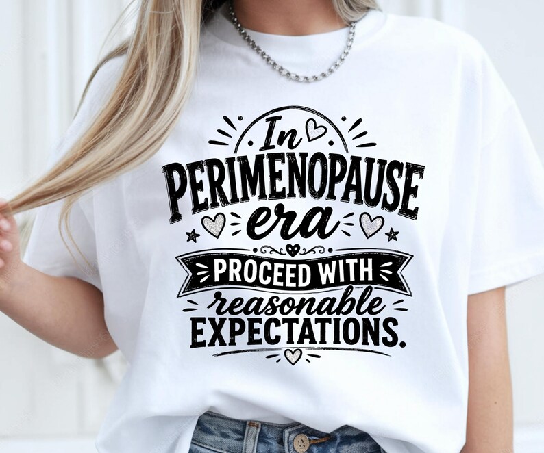 May include: A white short-sleeved t-shirt featuring black text that reads In PERIMENOPAUSE era PROCEED WITH reasonable EXPECTATIONS. The design includes decorative elements such as small hearts, stars, and a banner graphic.