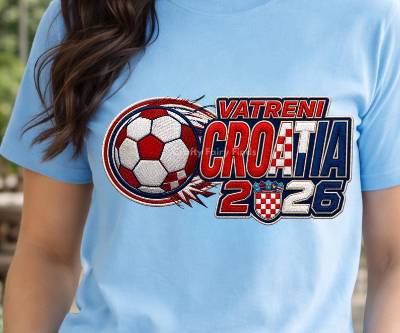 May include: Light blue t-shirt featuring a soccer ball with red and white accents, and the text "VATRENI CROATIA 2026". The design includes the Croatian coat of arms. The shirt is made of a soft material.