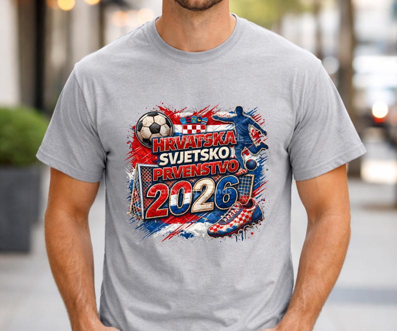 May include: A light gray t-shirt featuring a soccer-themed graphic. The design includes a soccer ball, a soccer player, a goal, and the text "HRVATSKA SVJETSKO PRVENSTVO 2026" in red, white, and blue, representing the Croatian flag.