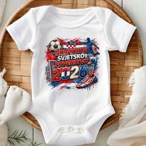 May include: White baby onesie with a soccer-themed graphic. The design features a soccer ball, a soccer player, a goal, and the text "HRVATSKA SVJETSKO PRVENSTVO 2026" in red, white, and blue. The onesie is short-sleeved.