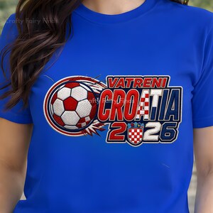 May include: A royal blue t-shirt featuring a soccer ball design with the text "VATRENI CROATIA 2026". The design includes the Croatian flag colors of red, white, and blue. The shirt is a crew neck style.