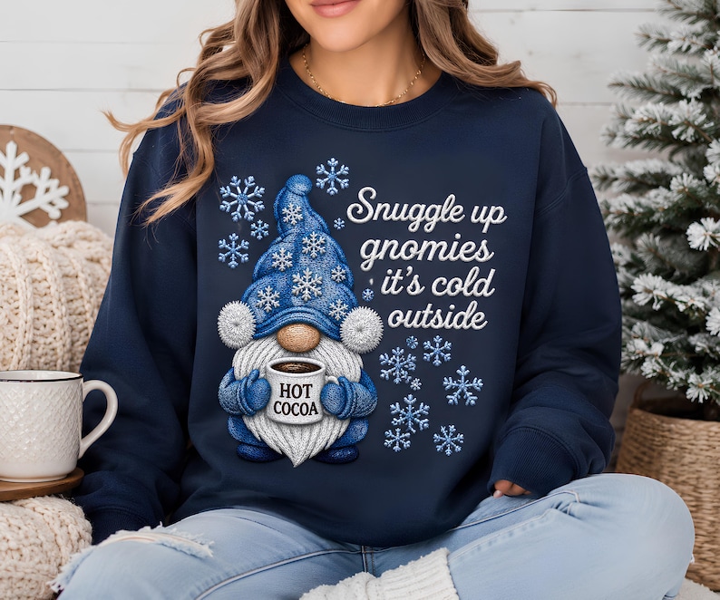 Snuggle Up Gnomies It's Cold Outside shirt and sweatshirt featuring an adorable blue winter gnome holding a hot cocoa mug surrounded by snowflakes. Available as a Gildan 100% cotton long sleeve shirt or 50/50 crewneck sweatshirt in a comfortable unisex true-to-size fit. Adult S–3XL with hoodies, youth, toddler and baby sizes available upon request. Design is a flat DTF print with a simulated embroidered appearance and is not actual embroidery or fabric stitching. Handmade and pressed to order.