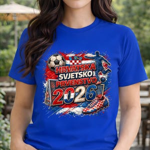 May include: A royal blue t-shirt featuring a soccer-themed graphic. The design includes a soccer ball, a player kicking a ball, a soccer shoe, and the text "HRVATSKA SVJETSKO PRVENSTVO 2026" in red and white, with a Croatian flag.