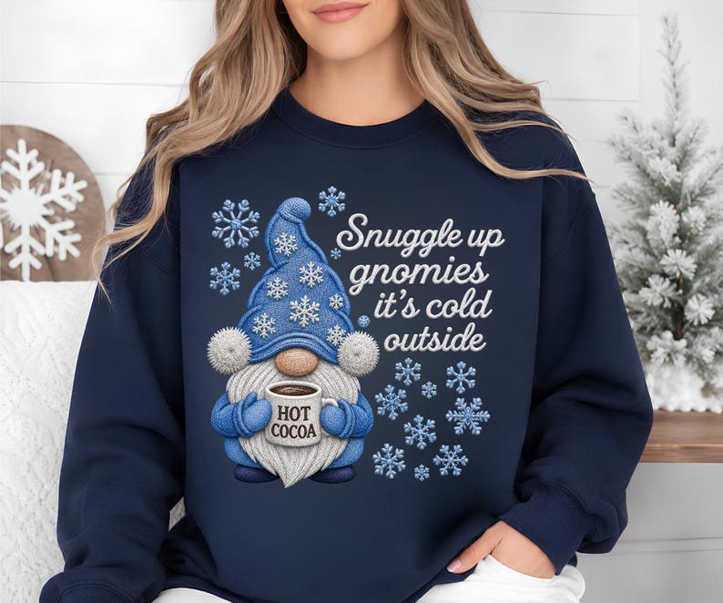 May include: A navy blue crewneck sweatshirt featuring a graphic of a gnome wearing a blue hat with white snowflakes. The gnome holds a mug labeled HOT COCOA. The text reads Snuggle up gnomies it's cold outside, surrounded by blue and white snowflakes.
