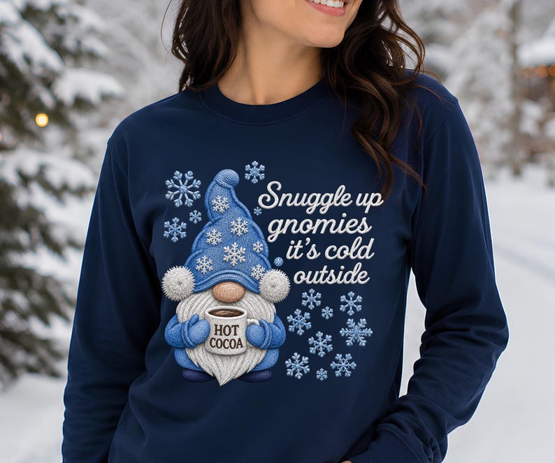 May include: A navy blue long-sleeve sweatshirt featuring a graphic of a blue gnome wearing a matching hat with white snowflakes. The gnome holds a white mug labeled HOT COCOA. The text reads Snuggle up gnomies it's cold outside.