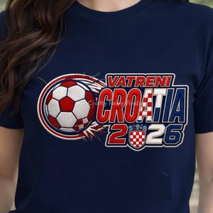 May include: Navy blue t-shirt featuring a soccer ball with red and white details, and the text "VATRENI CROATIA 2026". The design includes a Croatian flag emblem. The shirt is a sporty apparel item.