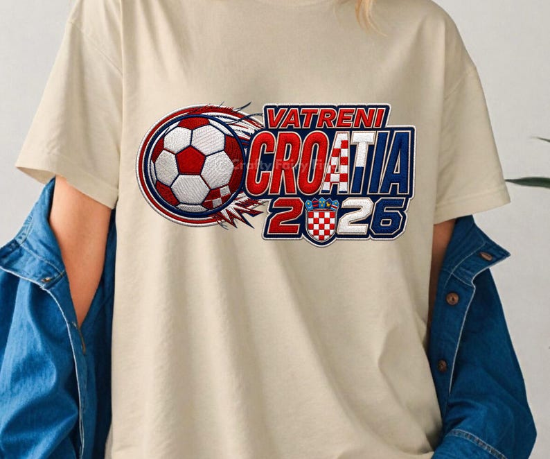 May include: Cream-colored t-shirt featuring a soccer ball graphic with red, white, and blue accents. The text "VATRENI CROATIA 2026" is displayed in a bold, stylized font, with the Croatian flag incorporated into the design.