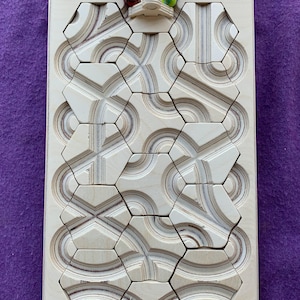 May include: Wooden puzzle board with the text "the Oort Cloud" at the top. The board features a series of carved hexagonal shapes and curved pathways. Colorful marbles are placed at the top of the board.