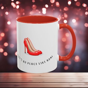 May include: White ceramic mug with a red rim and handle. The mug has a red high heel shoe illustration and the text "There's no place like home".