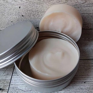 Puede incluir: Una lata de plata con tapa que contiene un producto blanco, cremoso y sólido. El producto también se muestra en una lata de plata separada, más pequeña.
