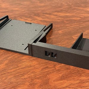 May include: Black metal rack mount component with multiple sections and mounting holes. The component has a rectangular shape with a flat base and vertical dividers. The letters "L4L" are cut out on the side.