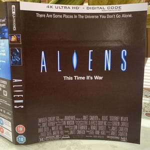 Può includere: Custodia Blu-ray 4K Ultra HD per il film "Aliens". La copertina è prevalentemente marrone scuro con il titolo "ALIENS" in lettere bianche e blu. Lo slogan "This Time It's War" è sotto il titolo. La custodia presenta anche i loghi della Twentieth Century Fox e la classificazione.