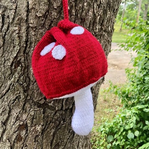 May include: A red and white knitted mushroom-shaped drawstring bag hanging from a tree branch.