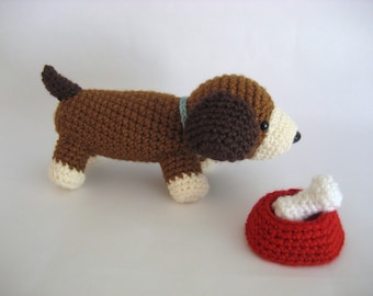 May include: A brown and white crocheted dog toy with a blue collar, looking at a red crocheted dog bowl with a white bone inside.