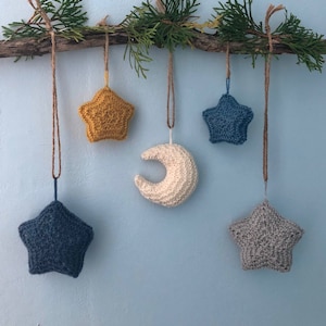 May include: Five crocheted ornaments hanging from a branch. The ornaments are a crescent moon, two blue stars, and two stars, one yellow and one grey.