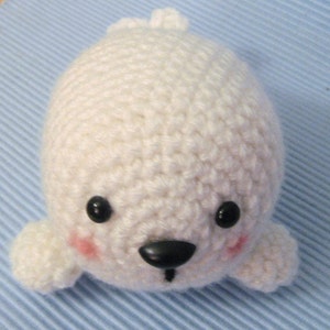 May include: White crocheted seal plush toy with black eyes, black nose, and pink cheeks.
