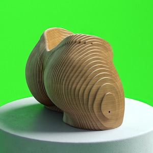 Może przedstawiać: Drewniana rzeźba buta, zbudowana z warstw drewna. But jest jasnobrązowy z widocznym usłojeniem i stoi na białym cokole na tle jaskrawozielonego tła. Projekt ma zaokrągloną piętę i spiczasty czubek.