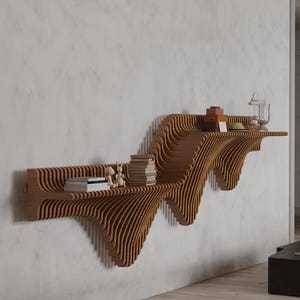 May include: A unique, wooden wall shelf with a wave-like design. The shelf is made of layered, light brown wood and holds books, decorative items, and a glass jar. The shelf is mounted on a white wall.