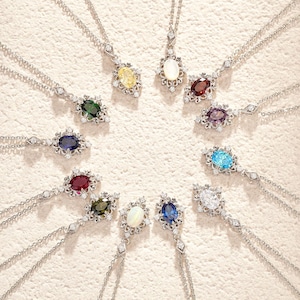 May include: A collection of silver necklaces, each featuring a different colored oval gemstone pendant. The pendants are surrounded by small, clear accent stones. The necklaces are arranged in a circular pattern.