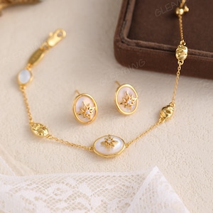 May include: A gold-toned jewelry set featuring a bracelet and matching earrings. The bracelet and earrings have oval-shaped white stones with starburst designs. The set is displayed on a white lace surface.