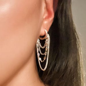 Pu&ograve; includere: Un orecchino d'argento con pi&ugrave; catenelle pendenti. L'orecchino &egrave; a cerchio con tre catene di diverse lunghezze. Le catene hanno piccoli elementi decorativi. L'orecchino &egrave; indossato sull'orecchio.