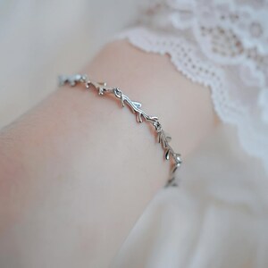 May include: A silver bracelet with a delicate design of interconnected branches and leaves.