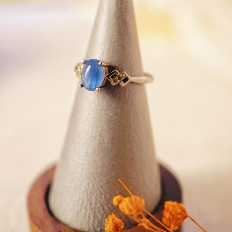 May include: A silver ring with a blue oval gemstone and smaller clear gemstones on the band.
