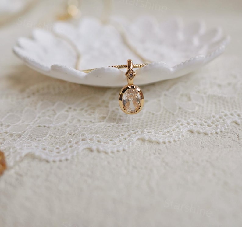 K&ouml;nnte beinhalten: Eine goldene Kettenkette mit einem klaren ovalen Anh&auml;nger mit einem kleinen Diamanten-Akzent.