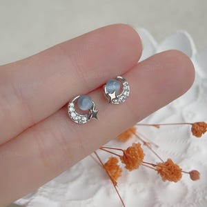 May include: A pair of silver crescent moon earrings with a small star charm and a light blue stone in the center of each moon.