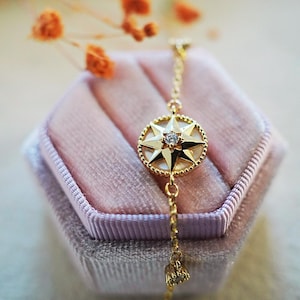 May include: A gold chain bracelet with a star-shaped pendant featuring a small clear stone in the center. The bracelet is displayed in a pink velvet box.