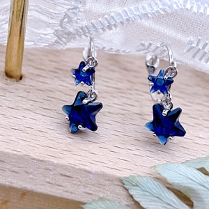 May include: A pair of silver dangle earrings with blue star-shaped crystals. The earrings have a clip-on closure.