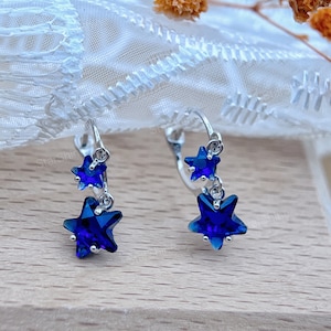 May include: A pair of silver dangle earrings with two blue star-shaped crystals on each earring.