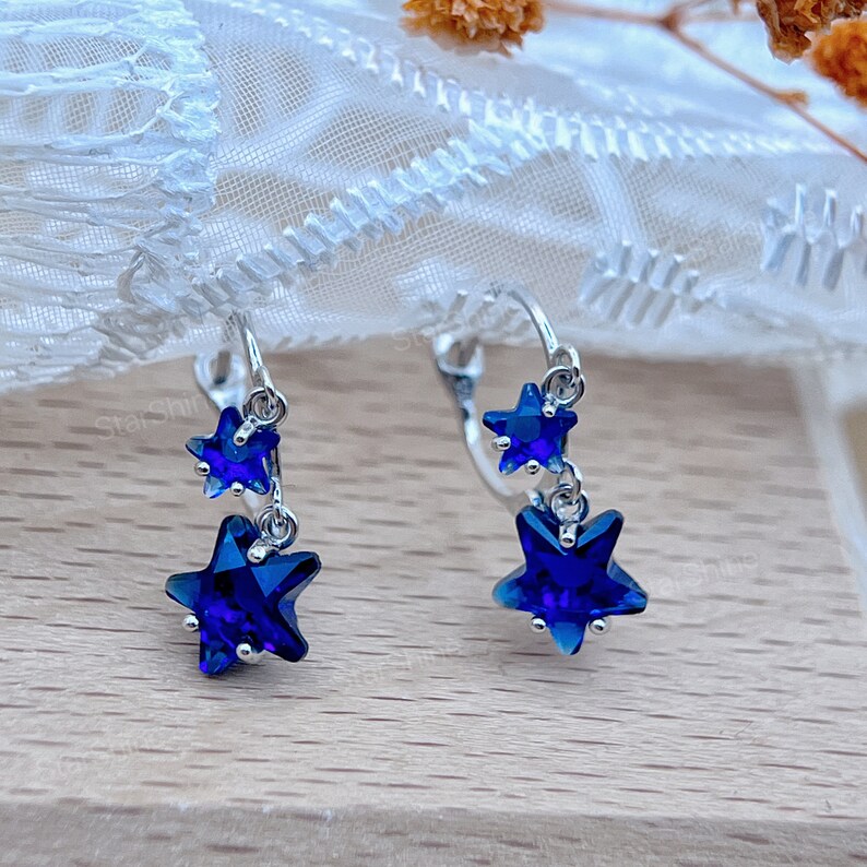 May include: A pair of silver dangle earrings with two blue star-shaped crystals on each earring.