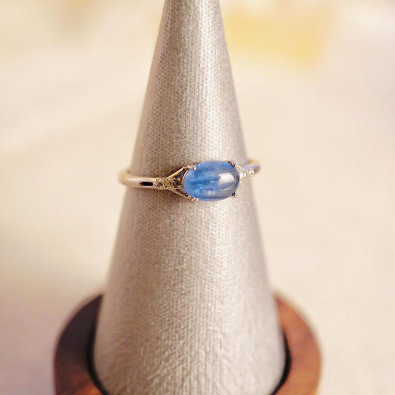 May include: A silver ring with a blue oval gemstone and small clear gemstones on the band.