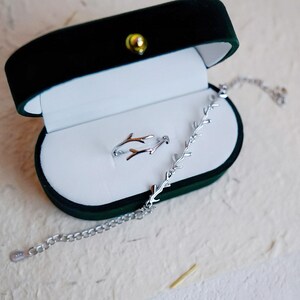 May include: A silver ring and bracelet set with a twig design. The jewelry is displayed in a green velvet box.