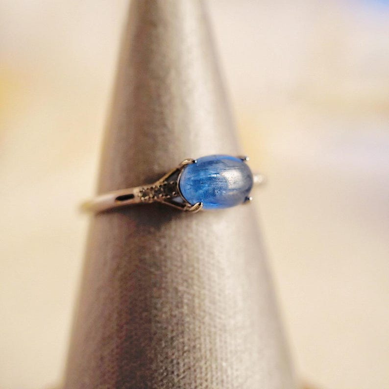 May include: A silver ring with a blue oval gemstone and small clear gemstones on the band.