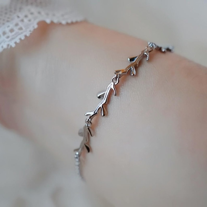 May include: A silver bracelet with a delicate design of branches and leaves. The bracelet is made of metal and has a simple, elegant look.